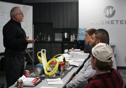 Image of older man standing, lecturing three other men, sitting down, in a room